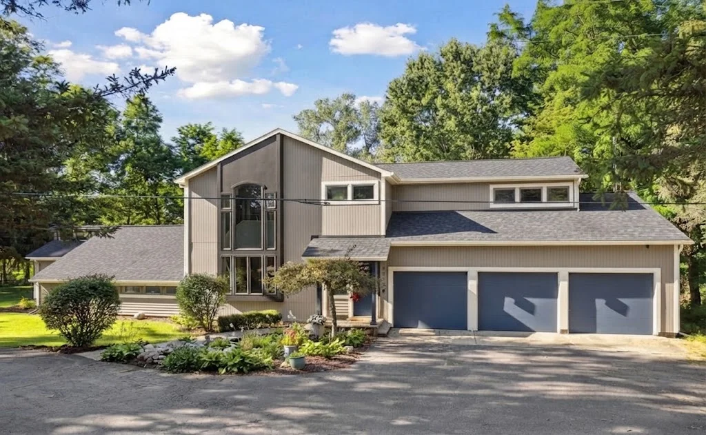 KI-Farbkonzept, das dasselbe Haus mit warmer greiger Fassade, anthrazitfarbenem Dach, warmweißen Zierleisten und dunkelblauen Türen zeigt